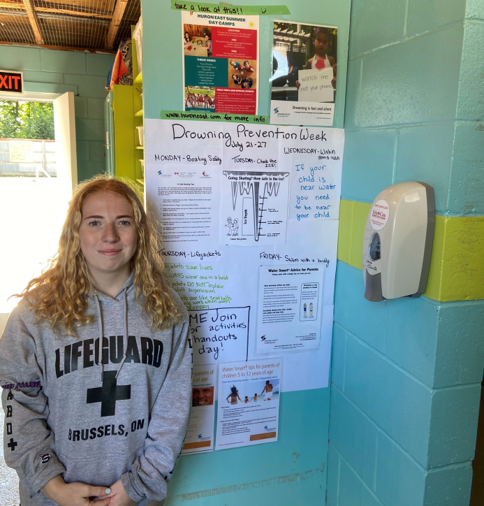 A picture of a summer student standing with a display she created for National Drowning Prevention Week.