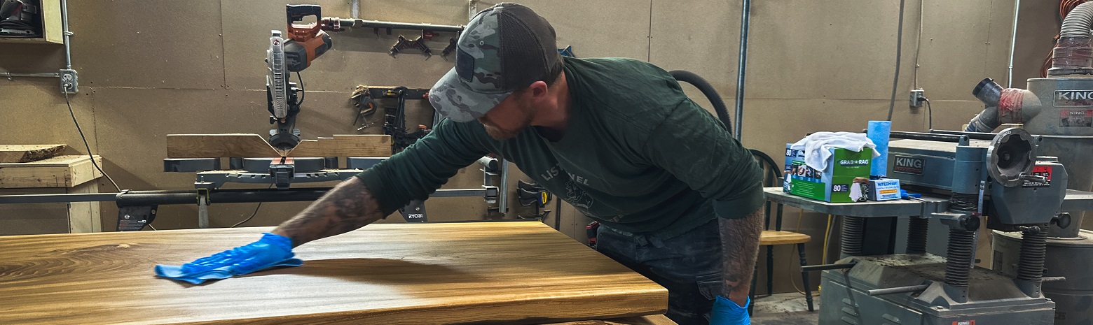 A picture of a young man finishing the top of a wooden table.