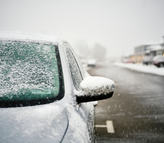 A picture of a grey car parked on the road with snow on it.