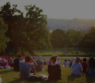 A picture of people outside sitting on a hill overlooking a park.